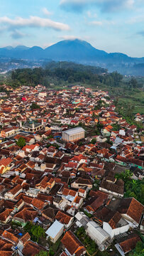 Aerial view of Ciwidey with dense terracotta rooftops nestled among lush green hills and mountains in Bandung, West Java, Indonesia.