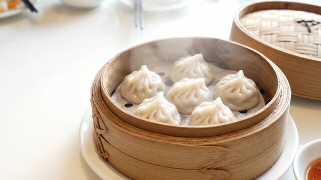 Steaming Asian dumplings in a bamboo basket. Freshly cooked dim sum served on a white table. Traditional cuisine and restaurant concept