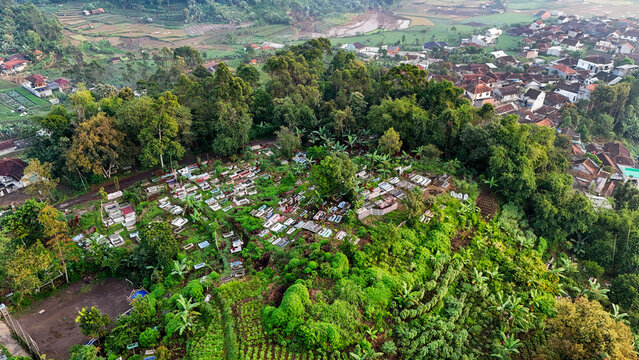 Aerial view of the Indonesian Muslim Cemetery Complex nestled on a lush green hillside surrounded by terraced fields and village houses in Ciwidey, West Java, Indonesia.