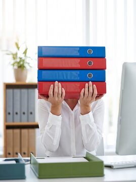 Businesswoman holding stack of colorful office folders hiding her face