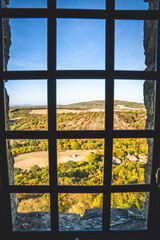 Fototapeta premium Scenic autumn landscape view framed by a medieval castle window grate. Sunny rolling hills and golden autumn trees seen through a dark iron window frame.