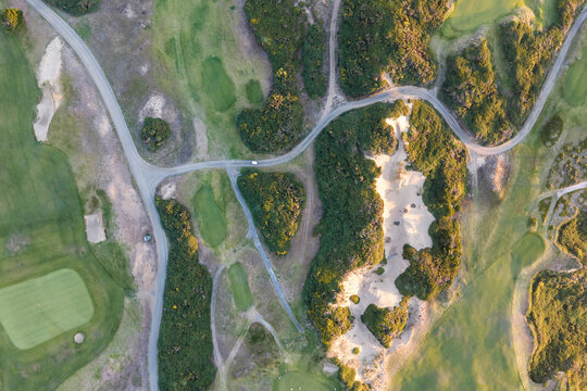 Aerial view of a coastal golf course in Bandon, Oregon, showing top down winding fairways, sand bunkers, natural dunes, and curving paths highlighted by golden hour light.