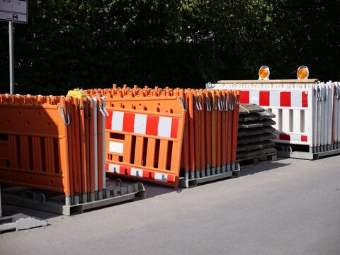 Road Construction Barriers and Traffic Safety Fence Panels Stacked on Steel Pallets beside Street and Green Hedges