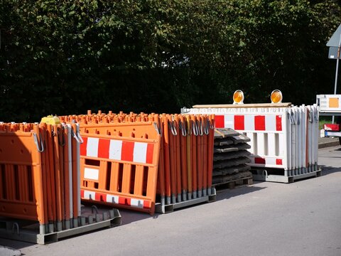 Stacked Plastic Traffic Control Barriers and Warning Lights Stored on Metal Transport Pallets beside Roadside Trees
