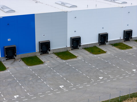 Aerial view of a modern logistics warehouse featuring multiple loading docks numbered 48 to 52, asphalt yard with parking spaces, and green patches in Gdansk, Poland.