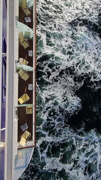Cruise ship sails through choppy green waters. White foam churns vessel wake. Passengers relax on open deck railings. Ocean spray splashes against ship side. Sunlight reflects off wet chair balcony