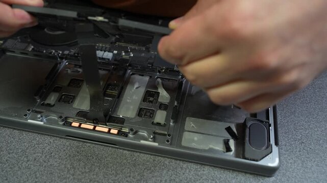 Technician removes internal cover to expose circuit board and cooling fans during laptop repair on a workbench