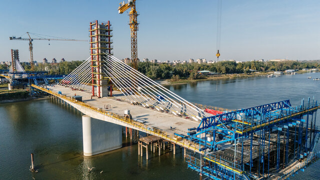 Aerial view of the cable-stayed bridge under construction over the Danube river with cranes and steel structures in Novi Sad, Vojvodina, Serbia.