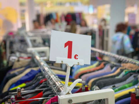Close view of 1 euro price sign above racks of second hand clothes in thrift store. Sustainability, circular economy, zero waste, thrift clothing, reuse and overconsumption concept