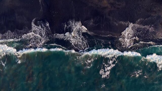 Aerial looking down at waves on a black sand beach in Bali Indonesia.