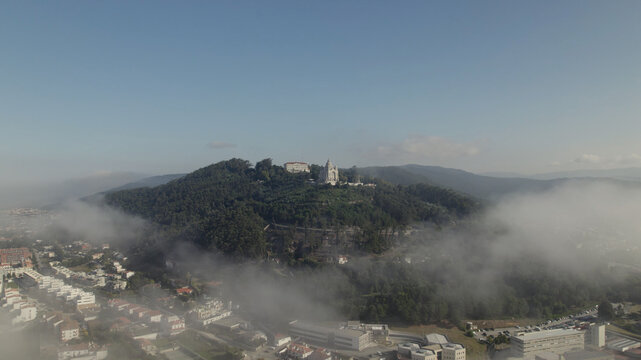 Aerial view of the Sanctuary of the Sacred Heart of Jesus perched on a hill surrounded by dense forest and morning mist above the city of Viana do Castelo, Viana do Castelo Dist, Portugal.