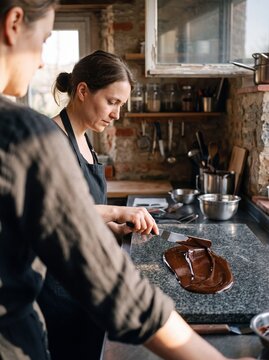 Artisan Chocolatier Woman Tempering Melted Dark Chocolate on a Marble Counter in a Rustic Confectionery Kitchen