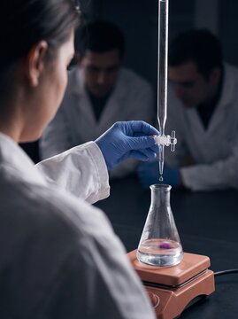 Female scientist performing chemical titration with burette and flask in laboratory while colleagues observe