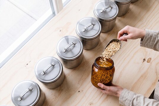 Person Pouring Rolled Oats into an Amber Glass Jar for Sustainable Kitchen Storage