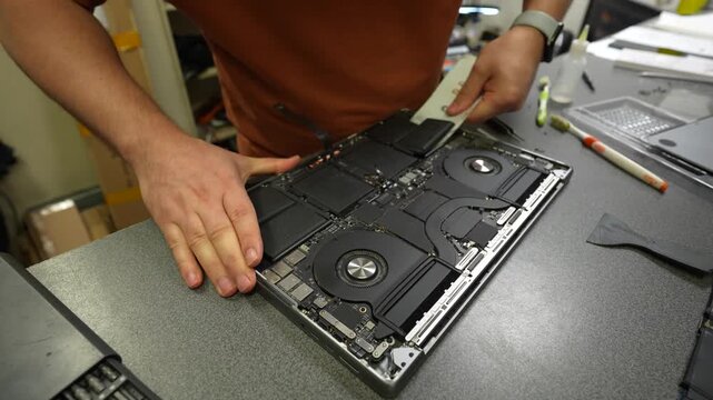 Technician opening laptop chassis and handling internal components during electronics repair on a workshop bench