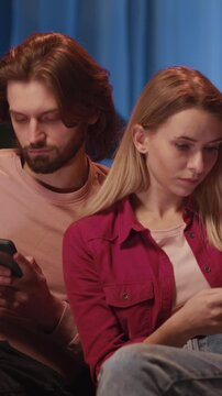 Internet addicted caucasian couple using mobile phones instead of real communications staying home looking at camera. Family portrait. Nomophobia.