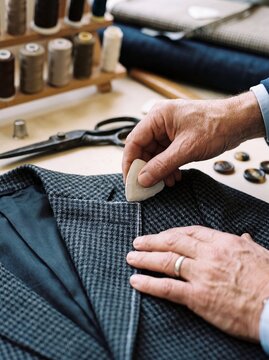Hands of a professional tailor marking wool fabric with chalk while tailoring a custom bespoke suit jacket in workshop