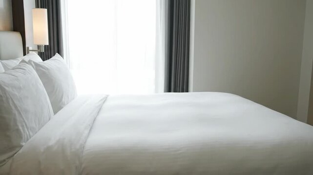 Fresh white hotel bedding in bright bedroom. Clean hotel room interior with made bed and sheer curtains. Hospitality and accommodation concept