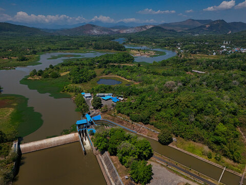 Aerial view of a dam structure on a river surrounded by lush green vegetation and distant mountains in Banjar Regency, South Kalimantan, Indonesia.