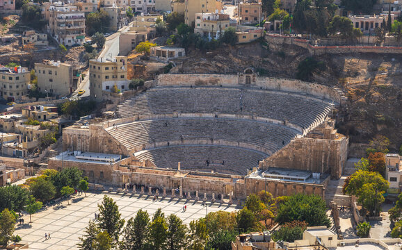 Aerial view of the Roman Theater with its ancient stone seating, stage area, and surrounding urban landscape with historic buildings and trees in Amman, Amman Governorate, Jordan.