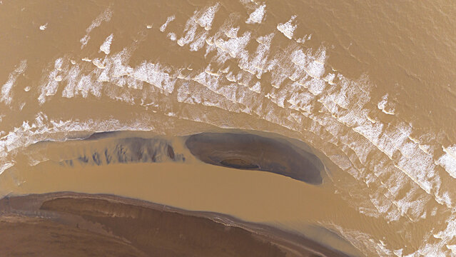 Aerial view of Dabhari Beach with gentle waves washing over the sandy shoreline and tidal patterns in the water in Surat, Gujarat, India.