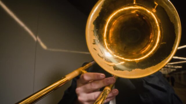 Caucasian young adult man playing trombone in slow motion with camera pulling back from brass bell. Ideal footage for urban jazz advertising, music school marketing, cultural promotions