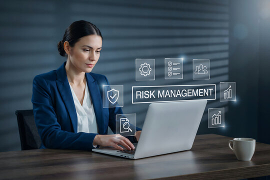 A businesswoman sitting at a wooden desk using a laptop with glowing holographic risk management and text floating in the dark office space