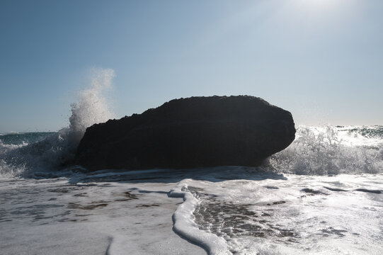 Sea surf on a coast with black stones in the water, viewed against strong backlight.