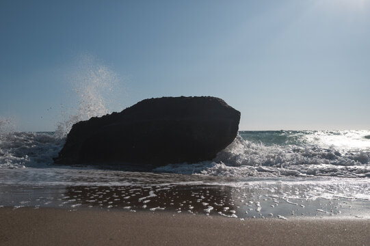Sea surf on a coast with black stones in the water, viewed against strong backlight.