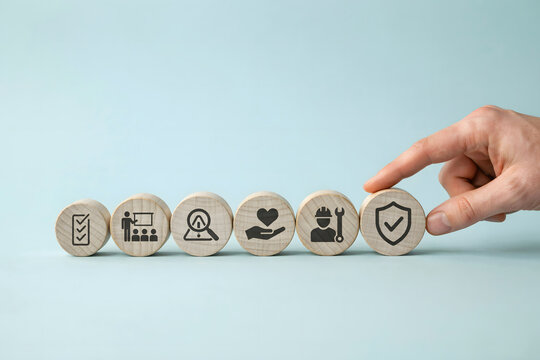 A hand placing a wooden block with a shield in a sequence of business including a checklist, meeting, search, heart, and worker
