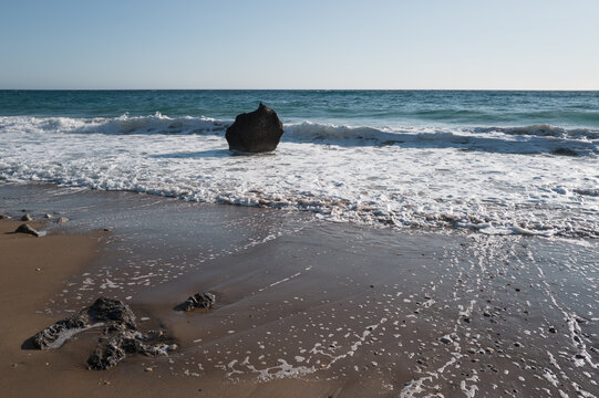 Sea surf on a coast with black stones in the water, viewed against strong backlight.