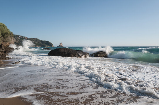 Sea surf on a coast with black stones in the water, viewed against strong backlight.