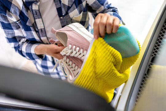 Person places pink sneakers into laundry machine
