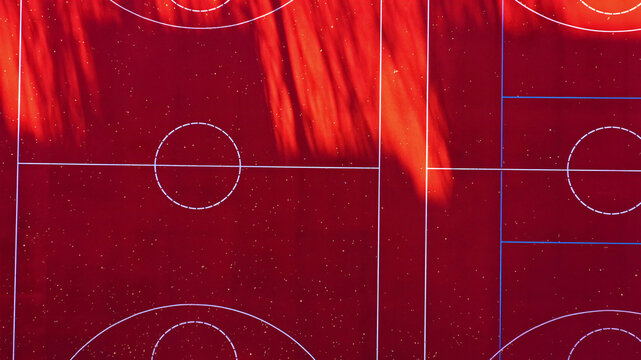 Aerial view of a vibrant red basketball court with white markings and geometric lines in Latvija.