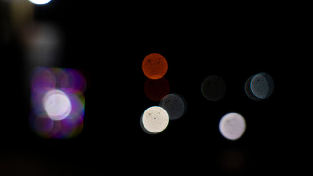 Soft bokeh lights glow against deep black night sky. Colorful orbs blur gently, suggesting urban street illumination. Dreamy, tranquil atmosphere evokes quiet, reflective moments