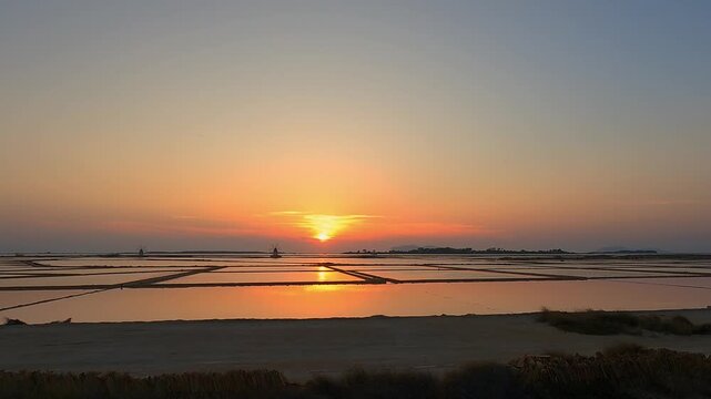 Golden sunset over tranquil salt pans near Trapani, Italy
