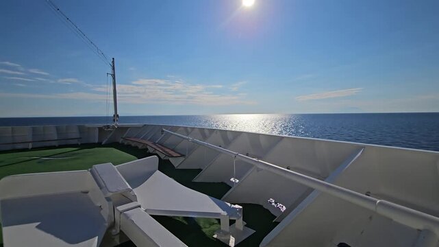 White anchor on green deck, ocean beyond. Sun glints off blue sea, clear sky above. Ship railings frame open water horizon
