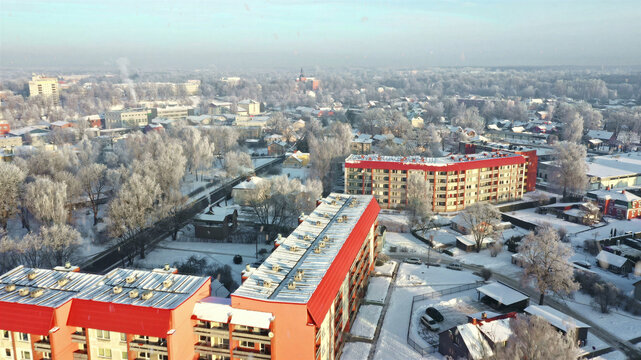 Aerial view of snow-covered residential area with distinctive red-roofed apartment buildings surrounded by frost-covered trees in Latvia.