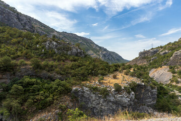 Fototapeta premium A scenic rocky canyon and valley with limestone cliffs, scrubby green hills and dry grasses beneath a clear blue sky. Rugged natural landscape suggesting hiking, geology, remote outdoors. Montenegro
