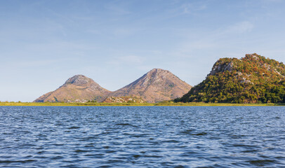 Landscape photo featuring Rijeka Crnojevica river in Montenegro. Scadar lake scene with blue water, distant rocky hills, and a wide blue sky. Perfect for nature, travel, and outdoor themes © evannovostro