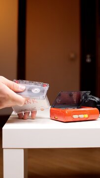 Person's hand inserting a transparent audio cassette labeled punk into an orange vintage portable cassette player on a white table, evoking nostalgia for 90s analog music media