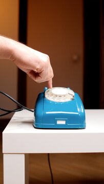 Person's hand dialing a classic blue rotary telephone, close up conveying retro communication, vintage analog technology, nostalgia, connection and old fashioned calling
