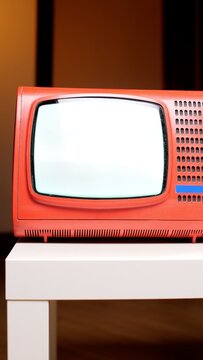 Red vintage television set with a blank white screen sitting on a white table, representing nostalgia, old technology, broadcasting, and classic entertainment