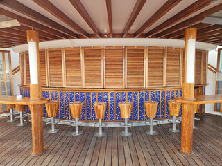 Wooden bar with rustic stools and blue tiled base. Beams and pillars frame open, airy cruise structure. Flooring matches bar warm, natural tones. Perfect for tropical, coastal, or beachside venues © Pavel Losevsky