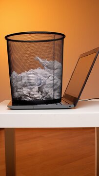 Trash can of crumpled paper on an open laptop keyboard representing digital cleanup, deleting files, information overload, digital detox and decluttering a modern workspace