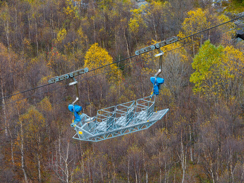 Aerial view of an industrial cable lift car suspended over a dense forest with vibrant autumn foliage in Tafjord, More og Romsdal, Norway.