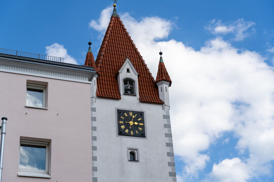 Historic clock tower stands among buildings under a blue sky with clouds