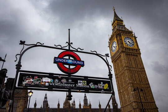 The entrance sign for Westminster Underground Station adorned with colourful stickers viewed near the Elizabeth Tower Big Ben in London England