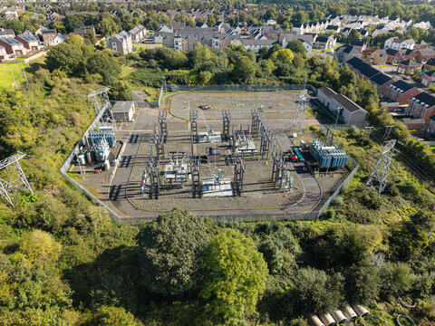Aerial view of an electrical substation with transformers and power lines surrounded by trees and residential housing in Lisburn, Northern Ireland, United Kingdom.