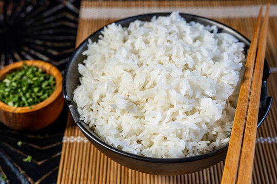 Jasmine white rice in a black ceramic bowl with chives and chopsticks 